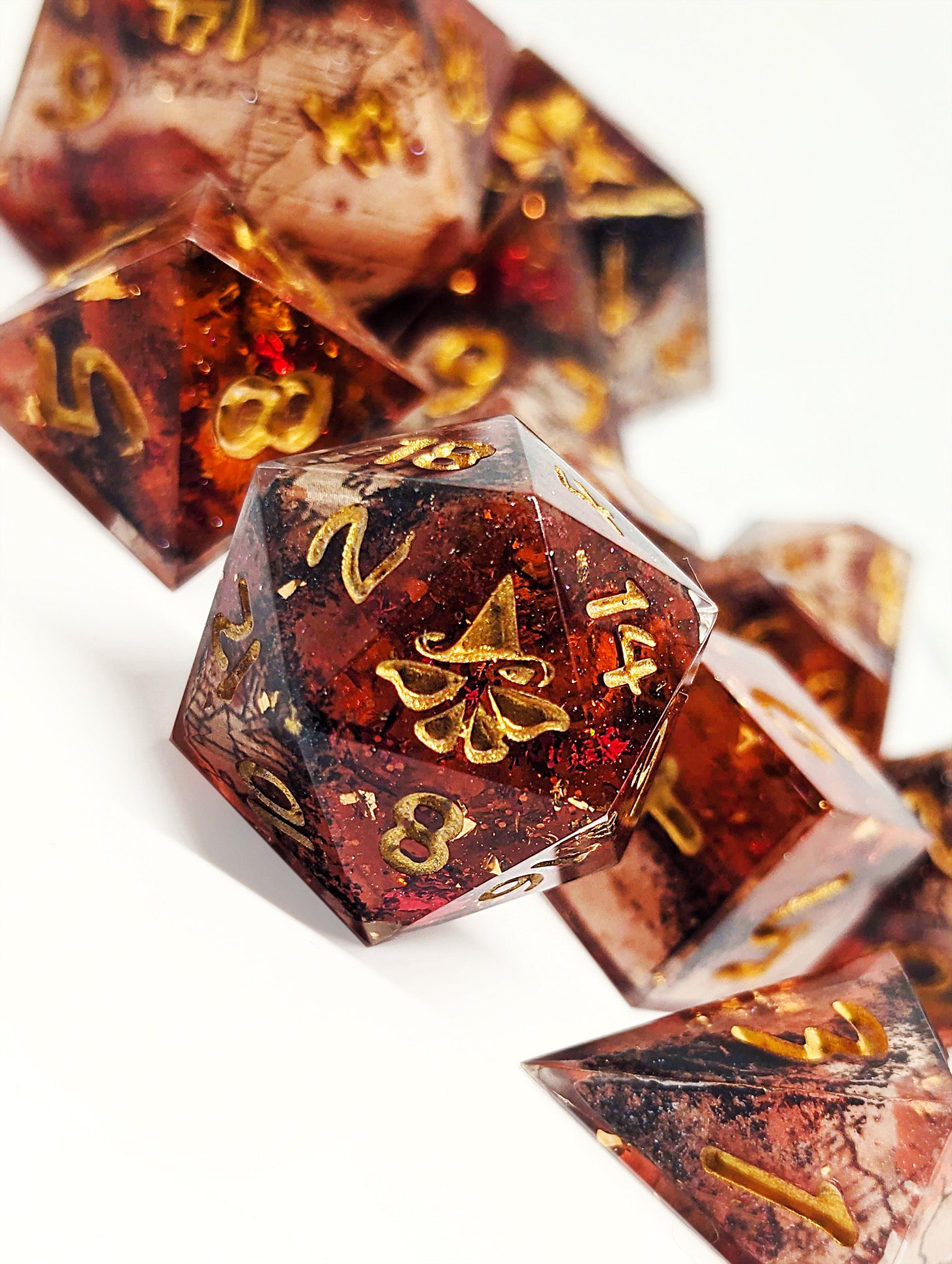 A set of polyhedral resin-cast dice numbered in gold with swirls of red and gold glitter.