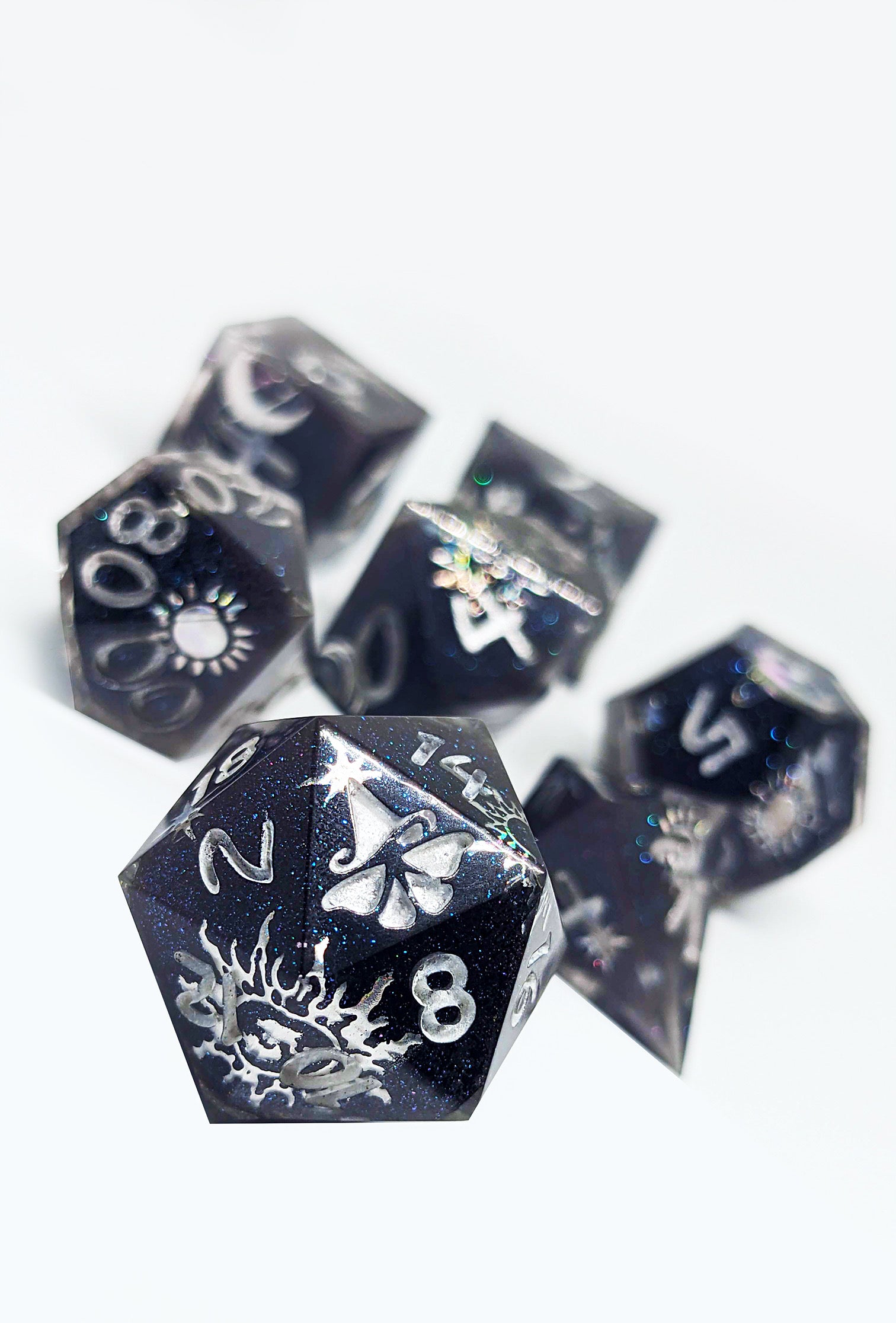 Set of deep blue and black polyhedral dice with white numbering and symbols on a white background.