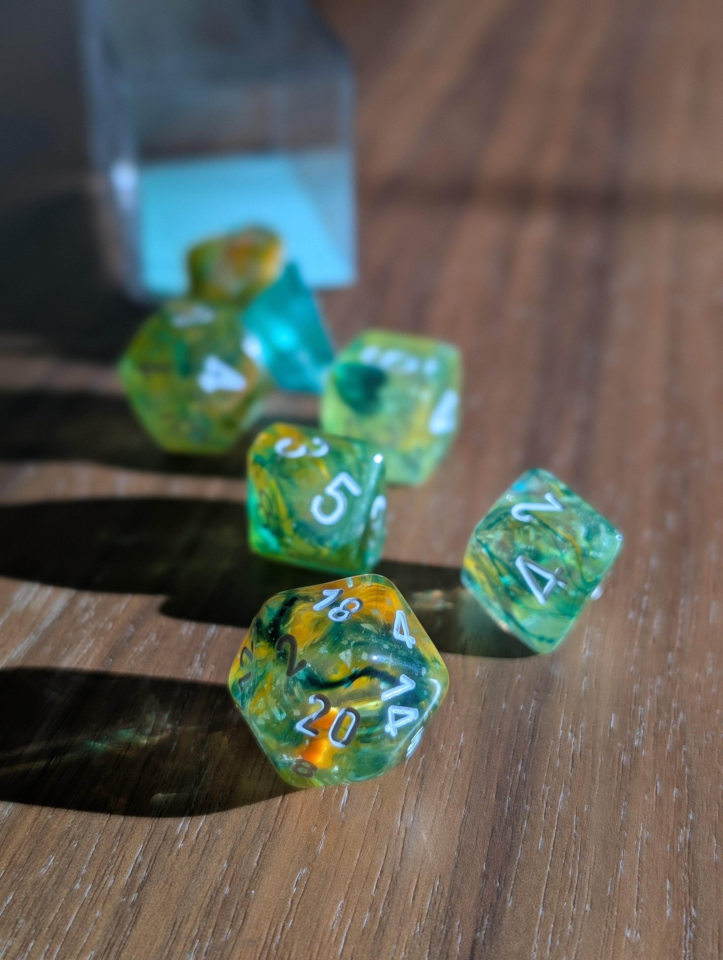 A set of translucent green polyhedral dice tumble out of a clear container toward the camera.