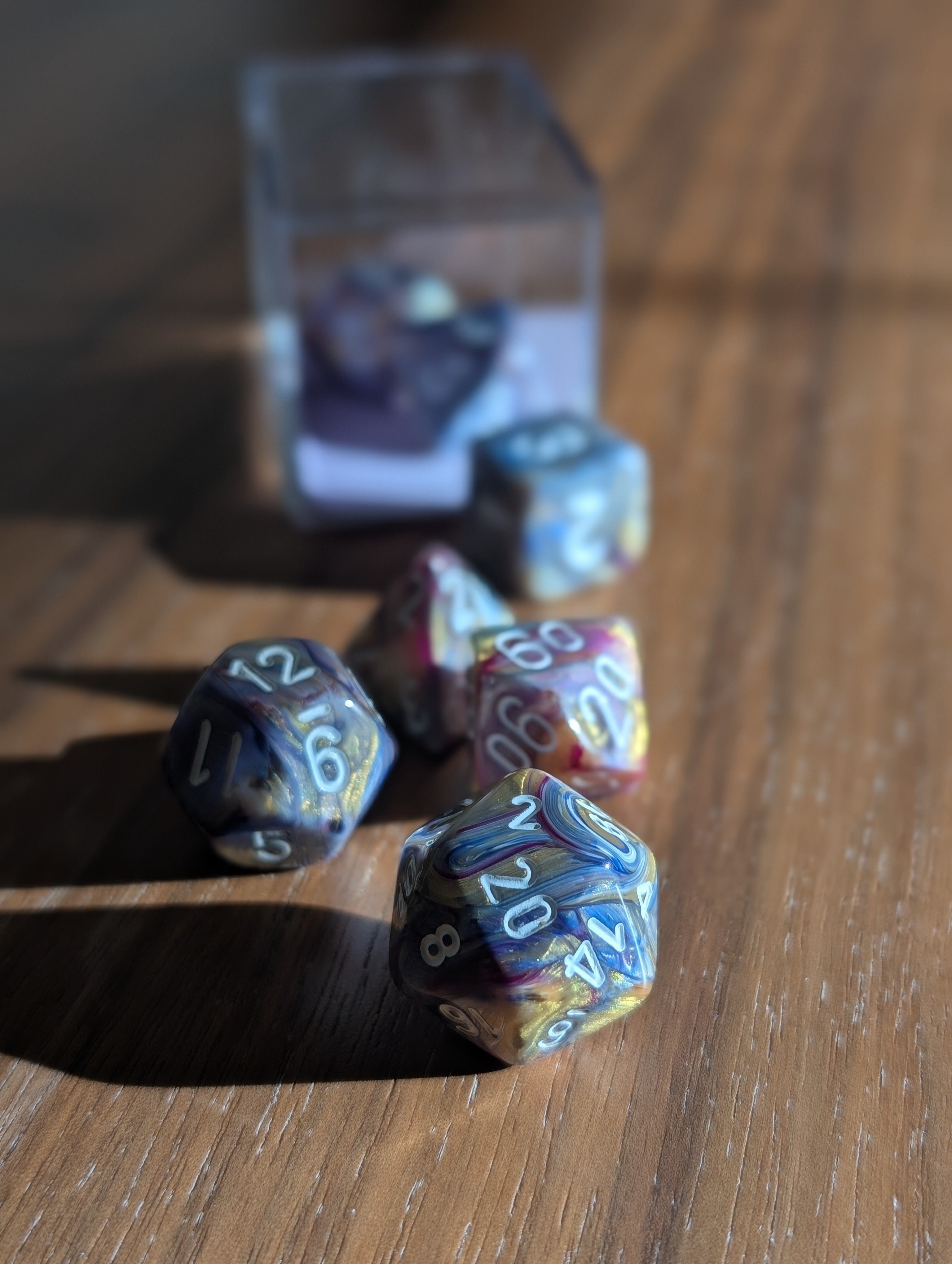 A set of ethereal polyhedral pearlescent dice in silver, blue, gold and purple spill out toward the camera.