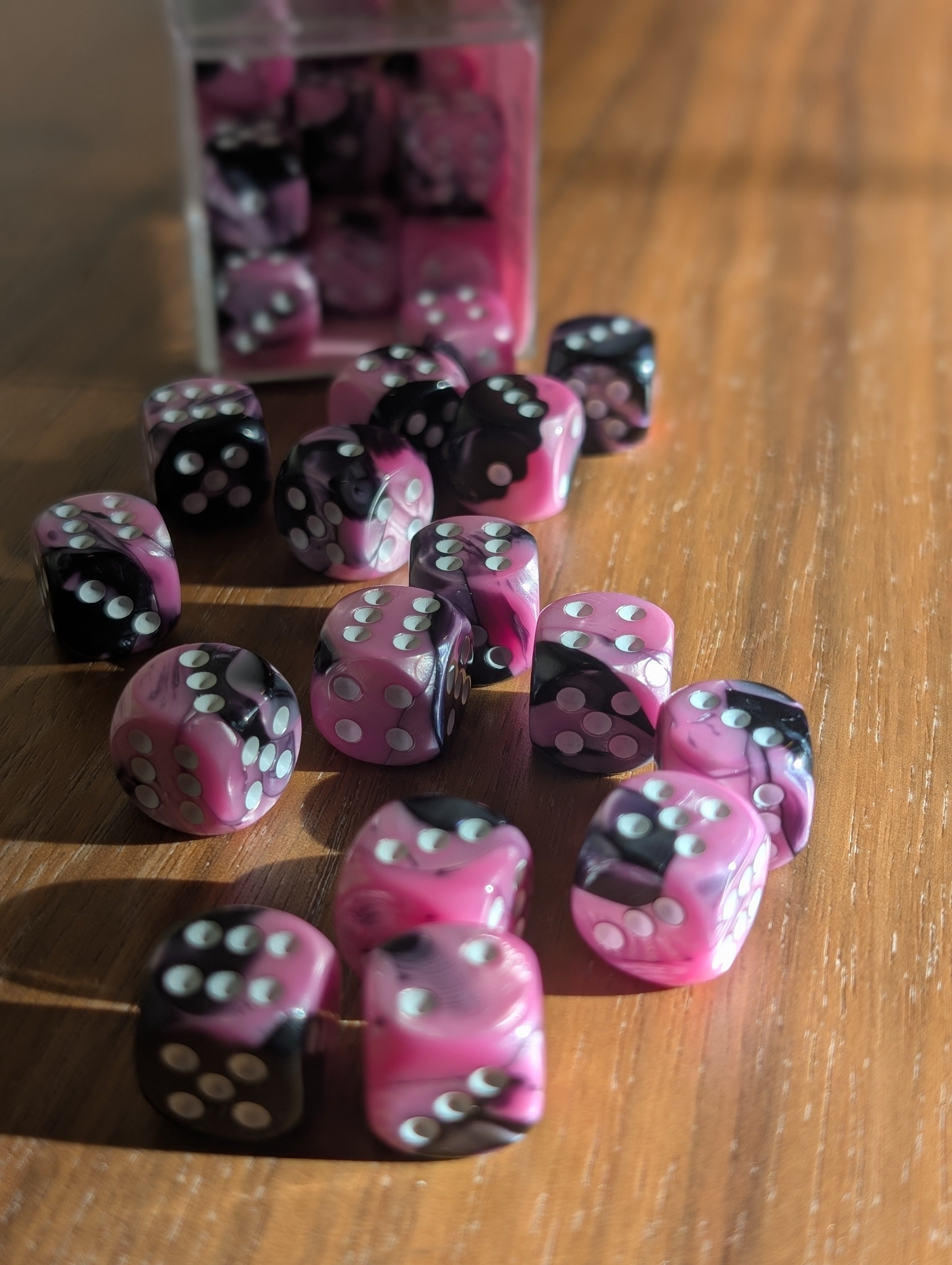A set of pink and black marbled dice spill out from a clear container toward the camera.