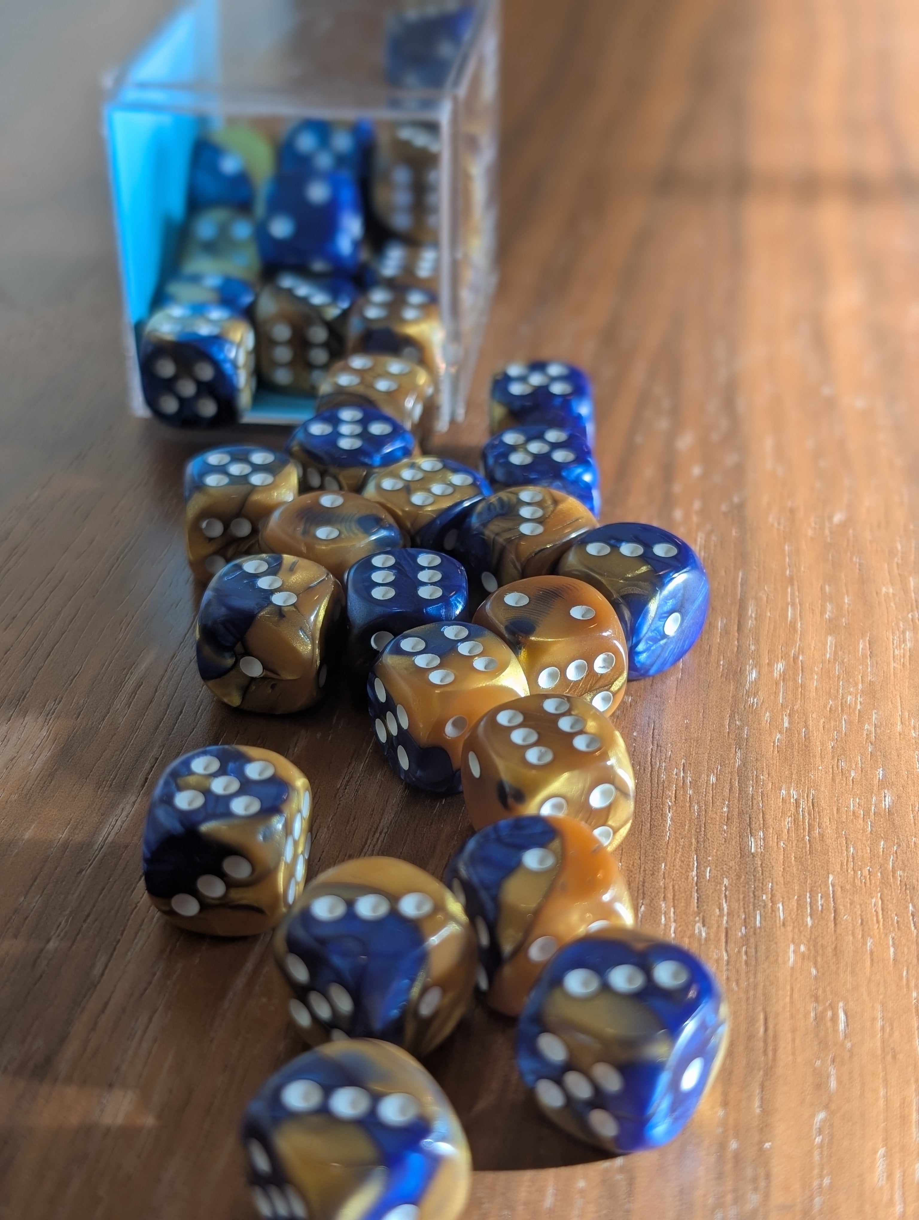 A set of blue and gold marbled dice spill out of a translucent container toward the camera.