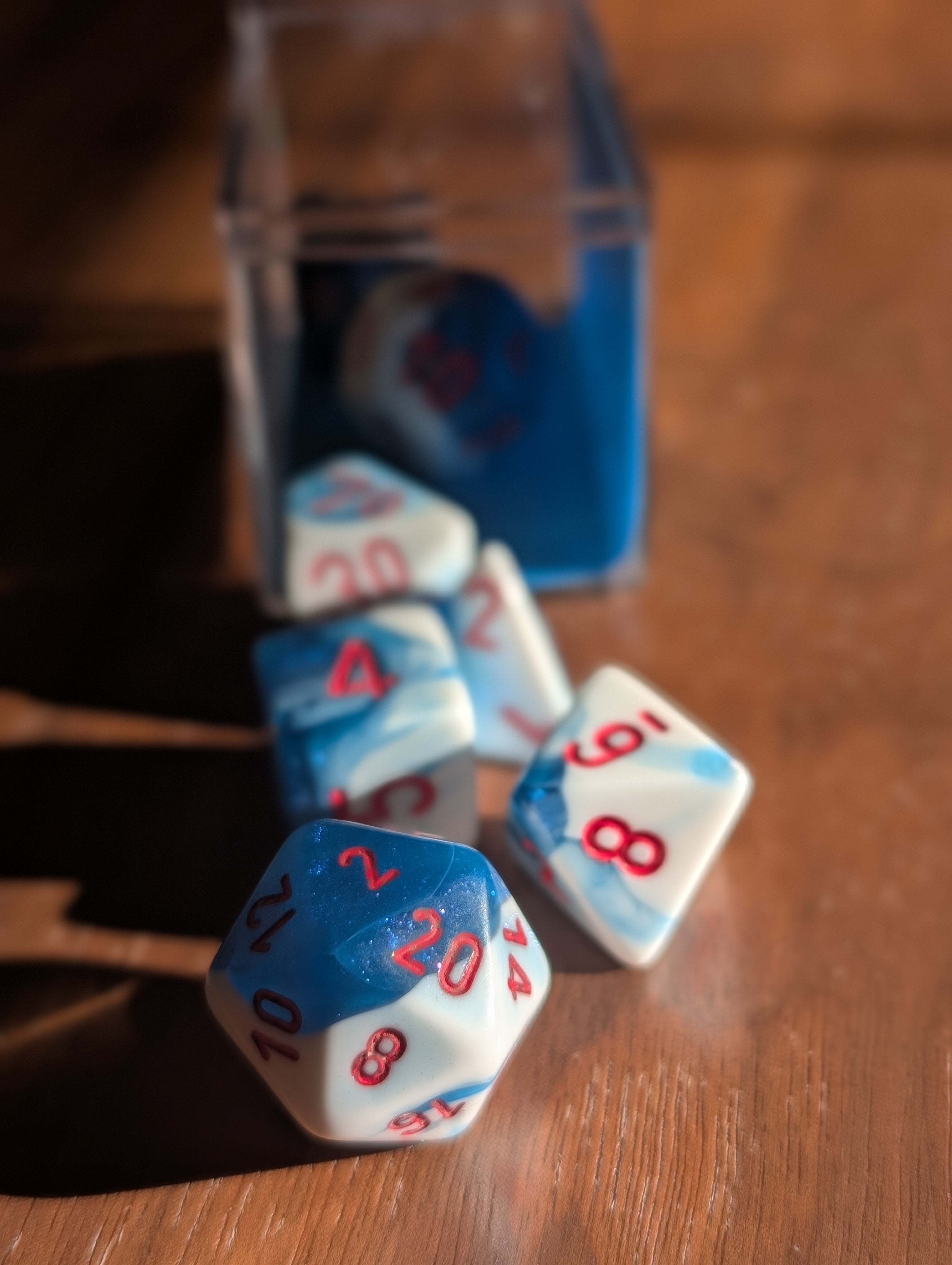 A set of milky white dice marbled through with glittering blue spill out of a translucent case toward the camera.